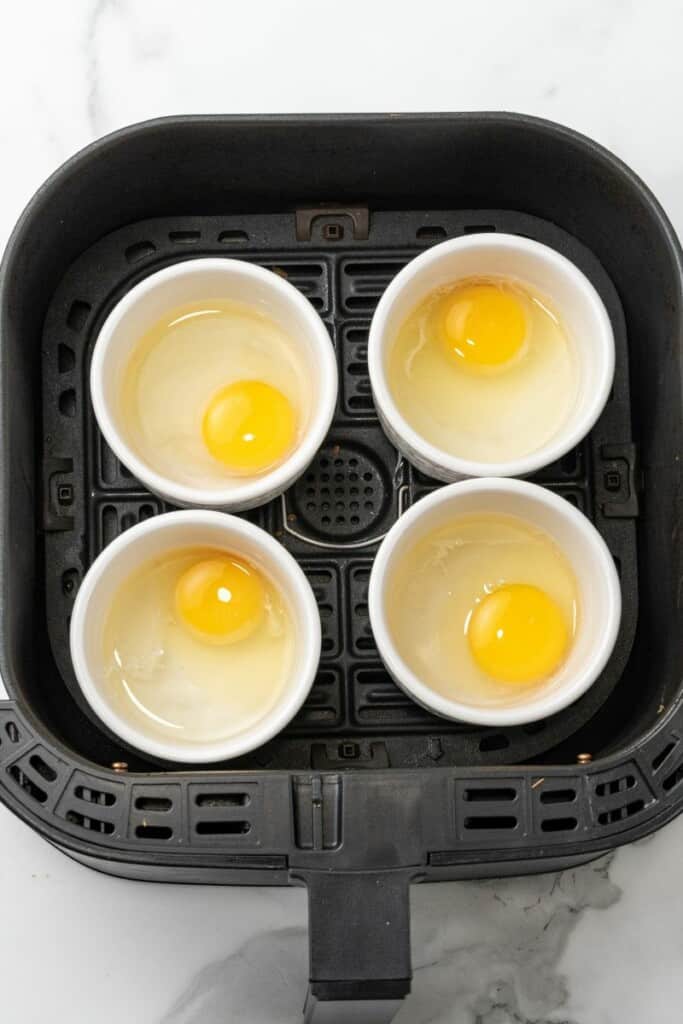 Ramekins filled with raw eggs, sitting in an air fryer.