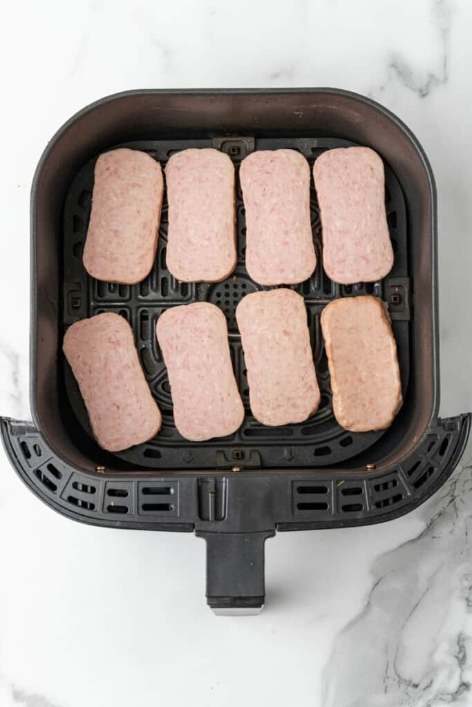 Adding slices of spam to air fryer basket.