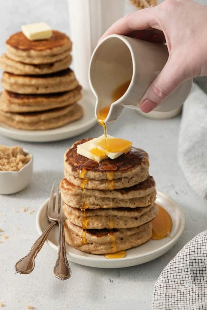 Pouring syrup onto stack of homemade pancakes.