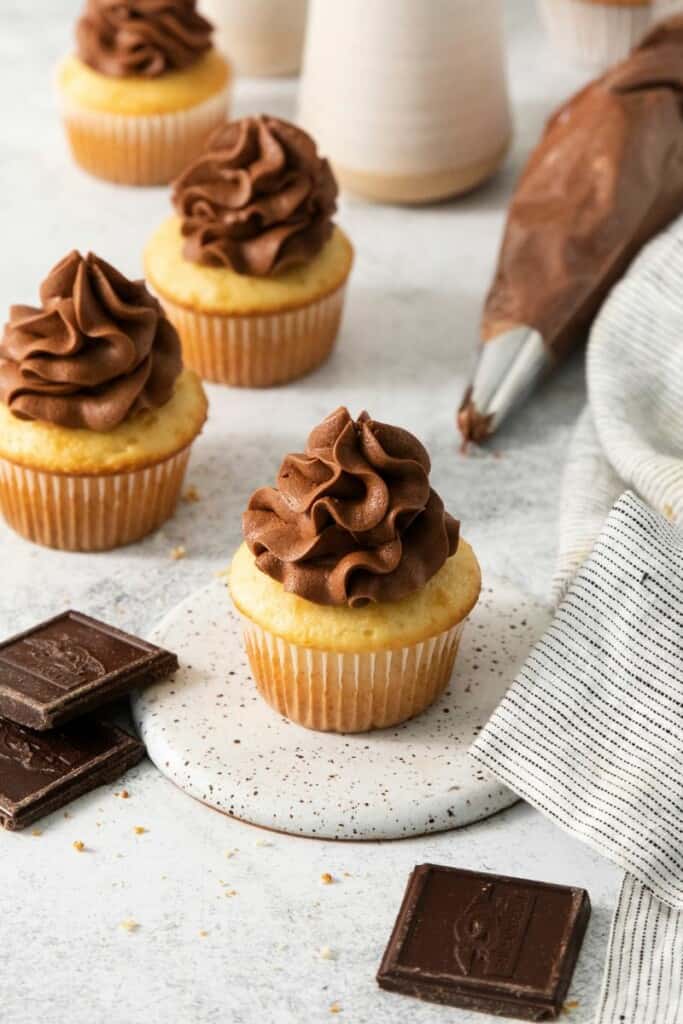 Piping bag filled with homemade cream cheese icing laid behind vanilla cupcakes.
