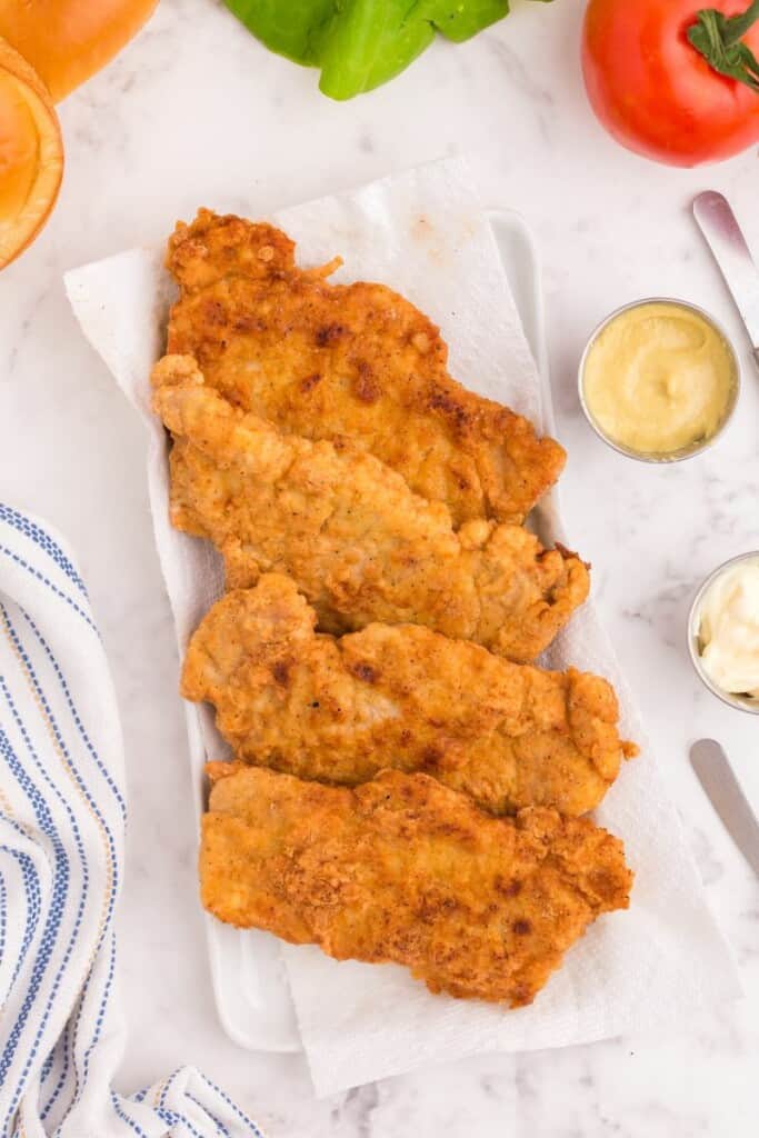 Freshly fried pork chops on a paper towel lined platter.