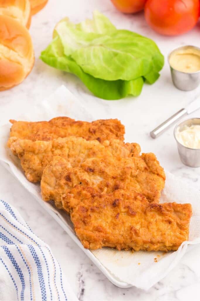 Fried pork chops on a platter with other ingredients in background.