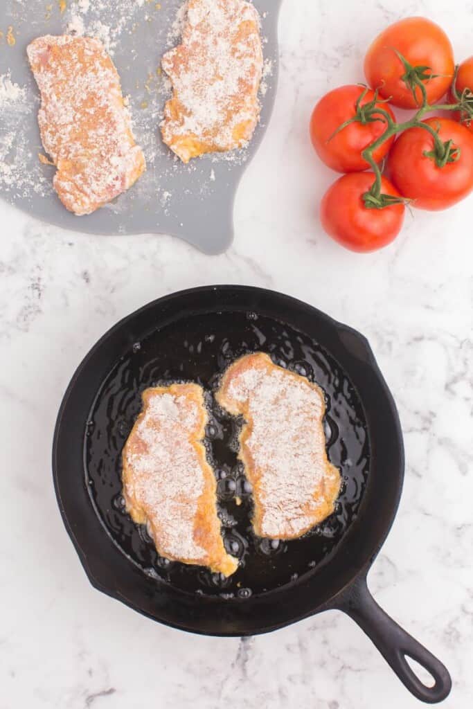 Frying pork chops in cast iron skillet with oil.