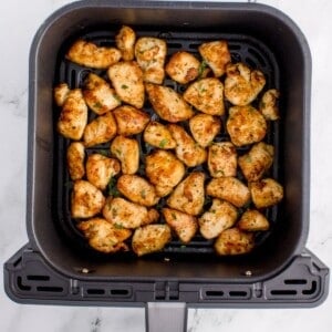 Cooked chicken bites in an air fryer basket.