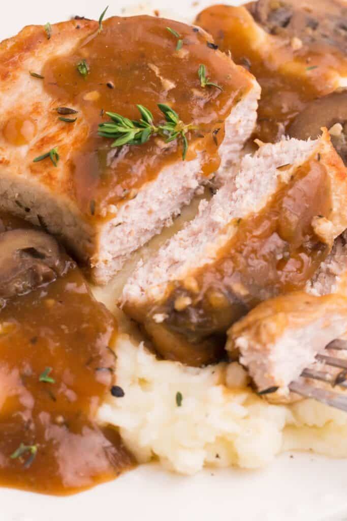 An Instant Pot pork chop covered in gravy cut open to see the tender and moist inside.