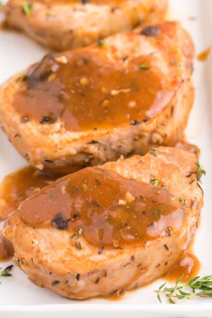 Instant pot pork chops close up on a white plate covered with the gravy from the pot.