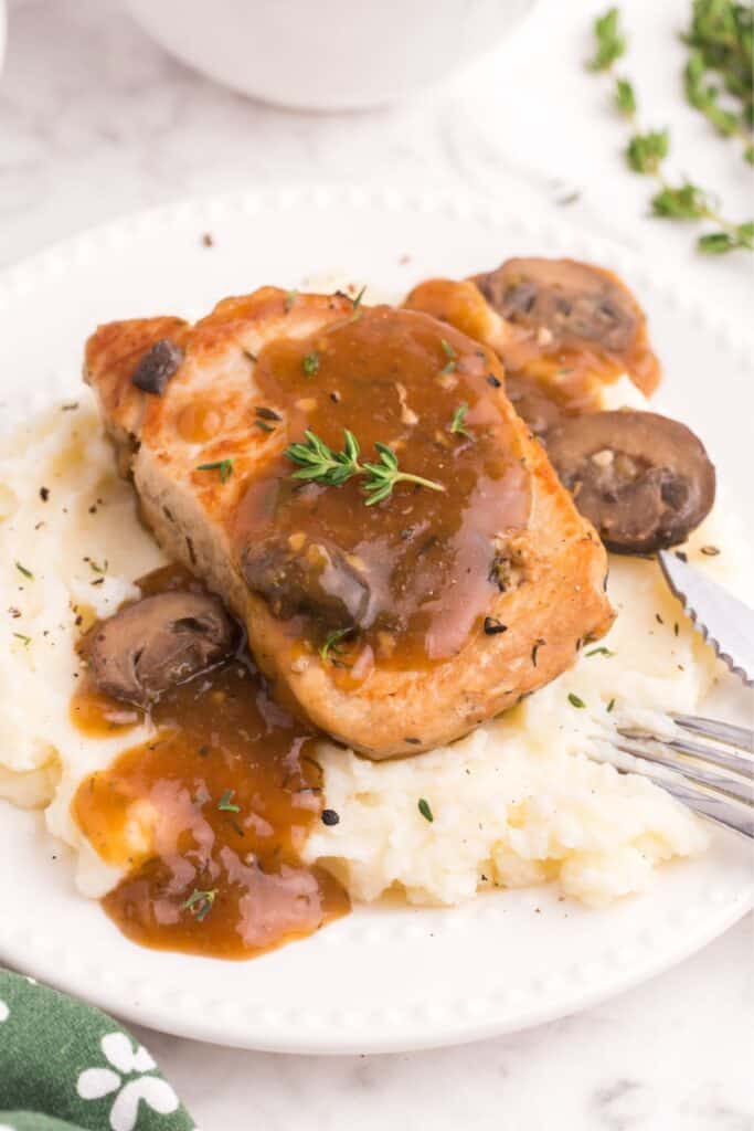 Instant Pot boneless pork chops covered in gravy served on top of mashed potatoes on a white plate.