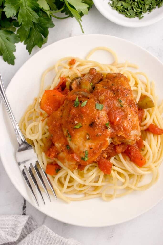 Serving chicken cacciatore over spaghetti on a white plate