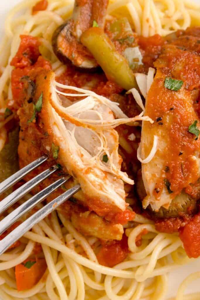 shredding boiled chicken in tomato sauce with a fork