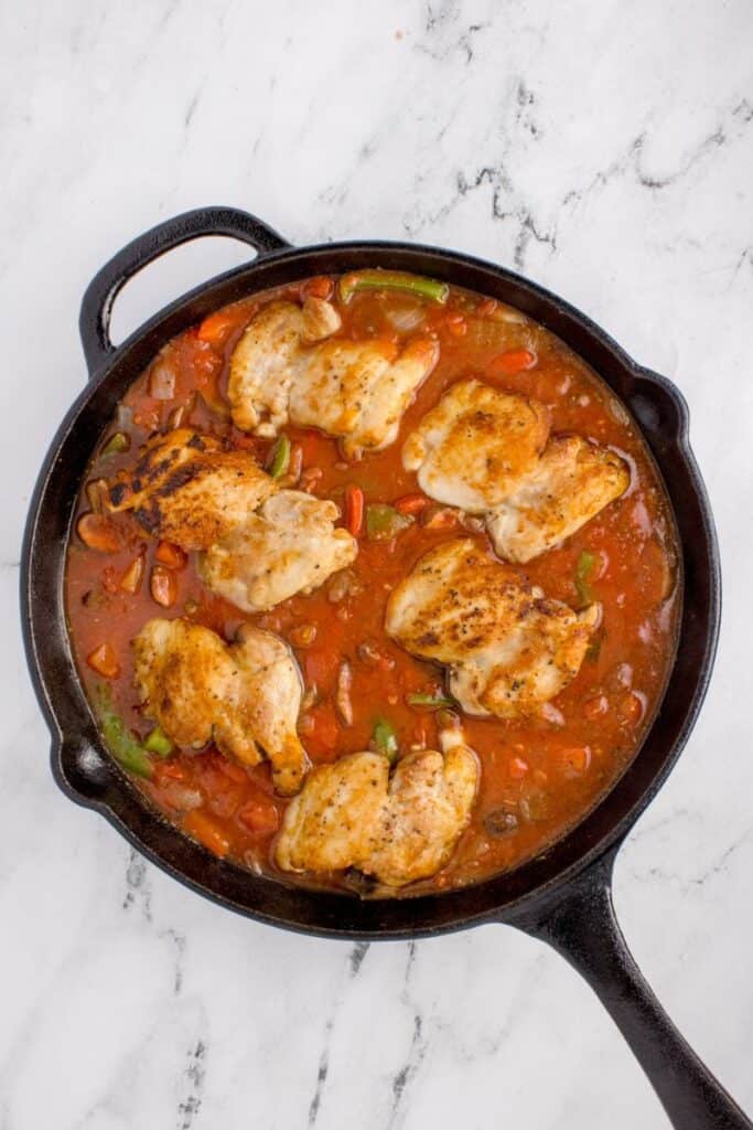 Adding seared chicken thighs to tomato and veggies