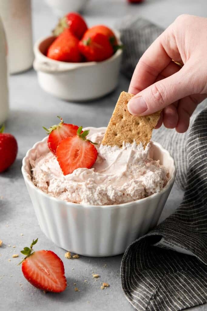 dunking a graham cracker into strawberry fruit dip