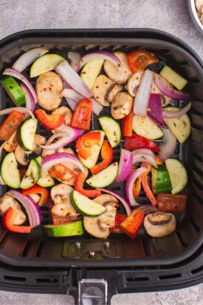Raw vegetables in an air fryer basket about to be cooked.