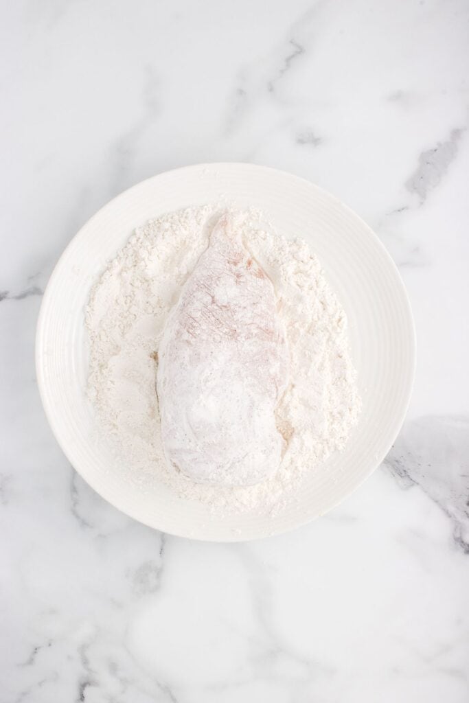 dipping raw chicken breast into flour