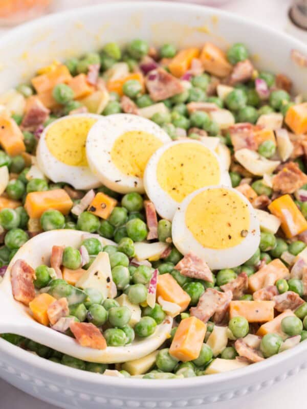 Close up with pea salad with eggs laying on top with a spoon about to scoop out a bunch.
