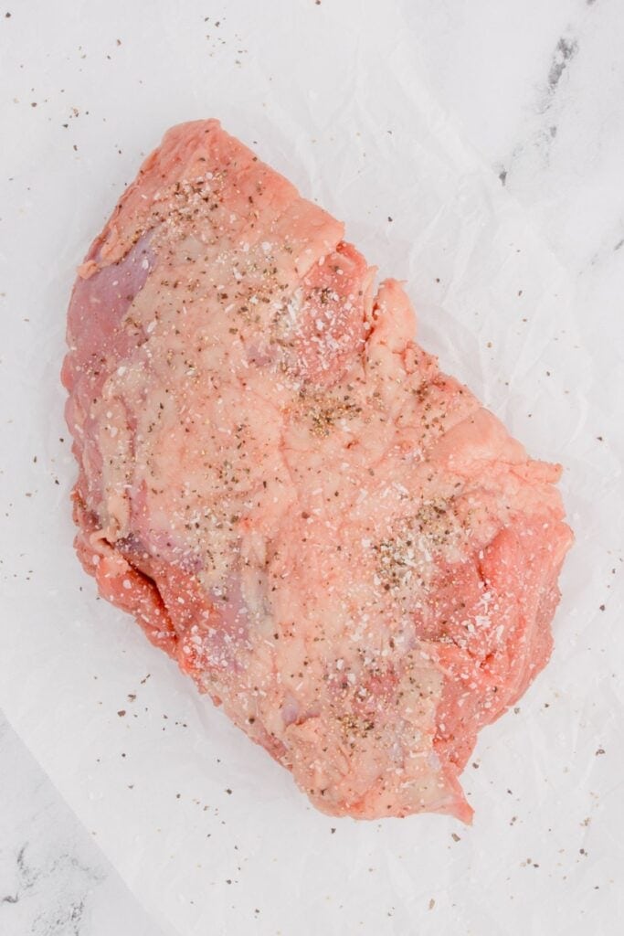 Raw sirloin tip roast with seasoning rubbed on it.