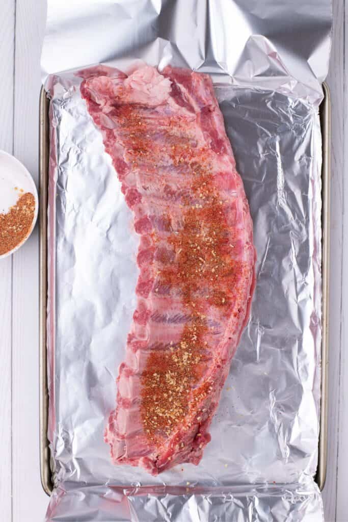 adding seasoned pork ribs to a basking sheet with aluminum foil