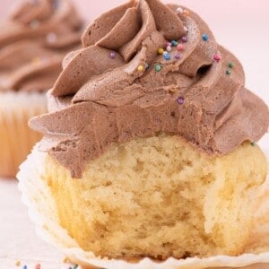 taking a bite out of moist vanilla cupcake with cocoa icing and rainbow sprinkles