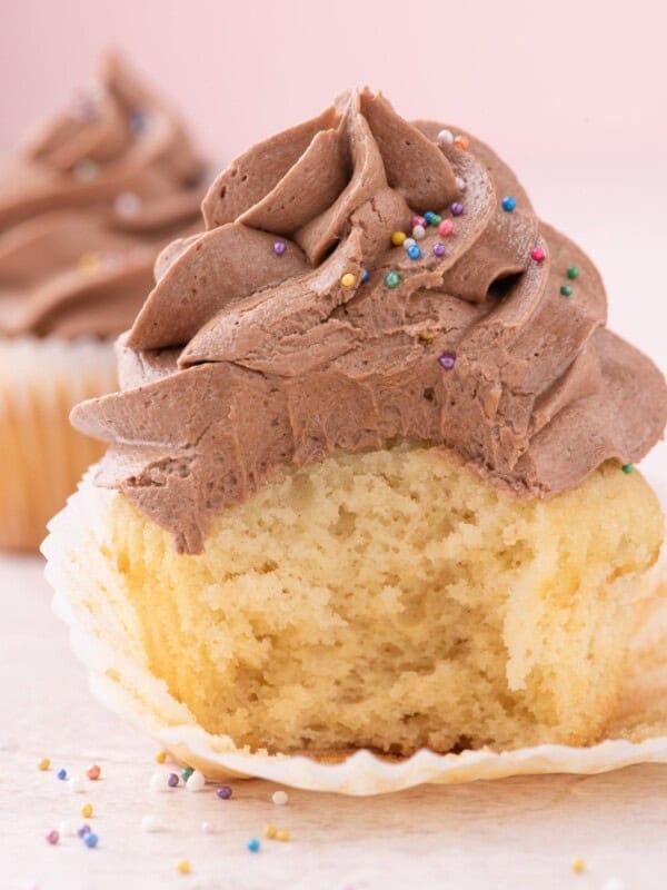 taking a bite out of moist vanilla cupcake with cocoa icing and rainbow sprinkles