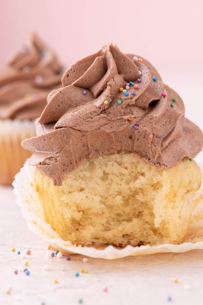 taking a bite out of moist vanilla cupcake with cocoa icing and rainbow sprinkles