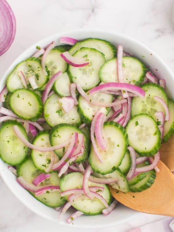 Closeup of the cucumber and onion salad in a serving bowl with wooden serving utensils.