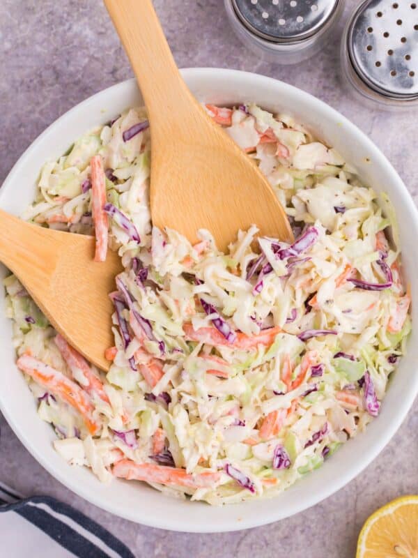 Easy coleslaw recipe in a white bowl with wooden utensils for serving.