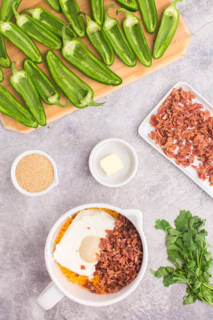 Jalapeno peppers cut in half with seeds and membranes removed, and filling mixed in a bowl to make baked jalapeno poppers.