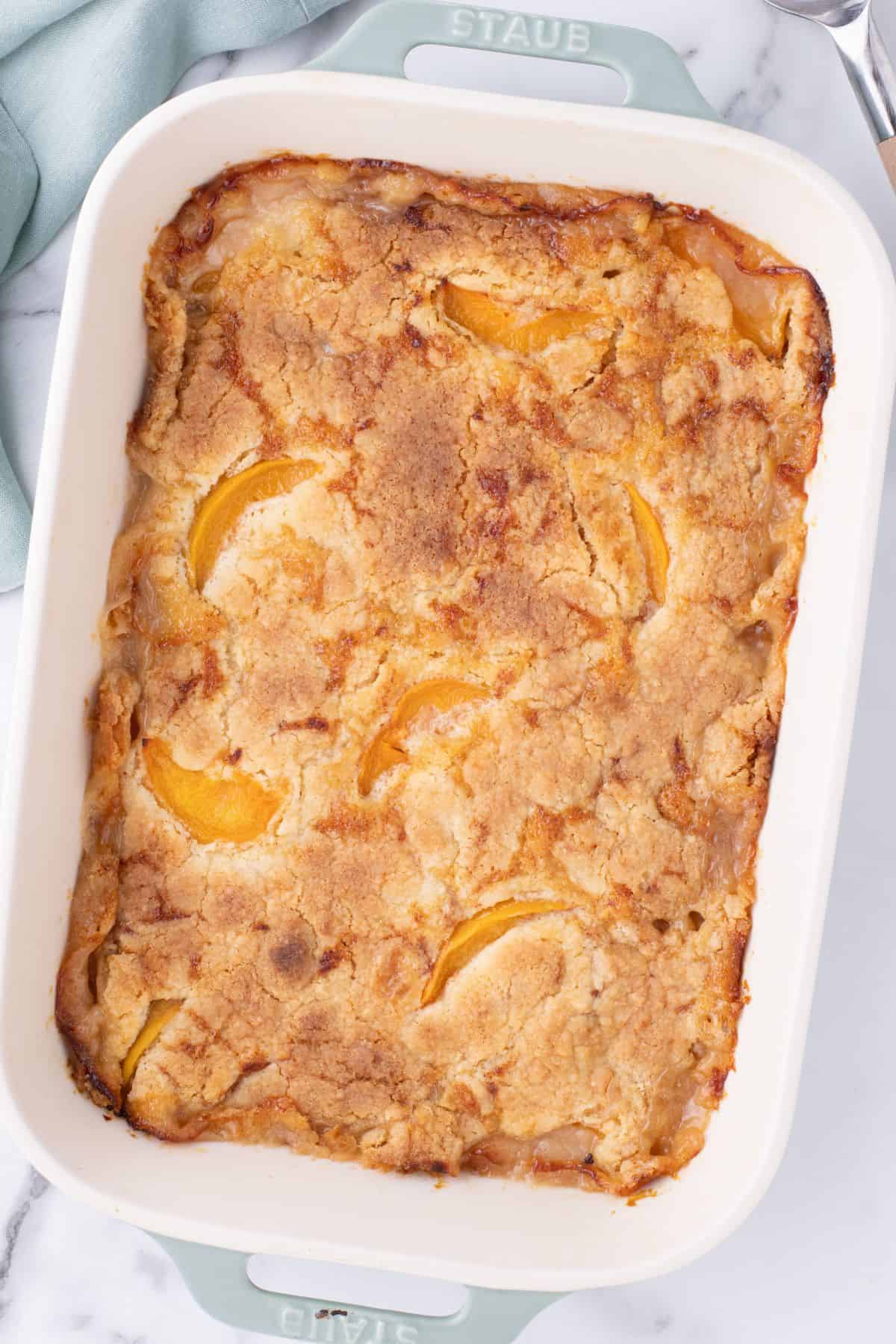 Top down view of the peach cobbler with cake mix in a baking dish out of the oven before being cut into.