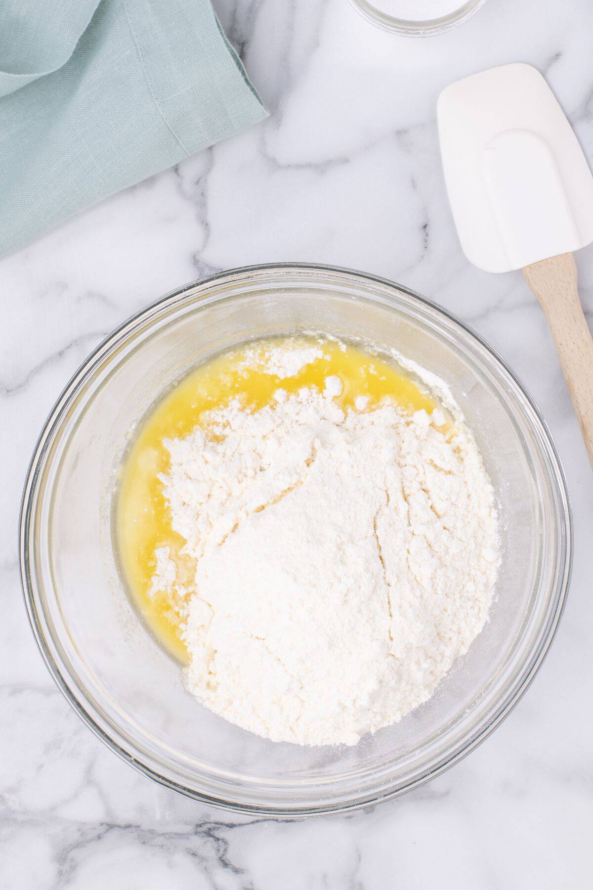 The melted butter with cake mix and cinnamon in a bowl about to be mixed with a baking spatula.