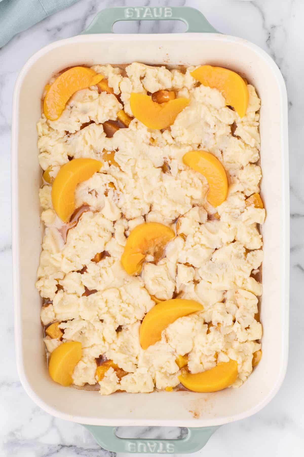 More canned peaches put on top of the peach cobbler right before going into the oven.