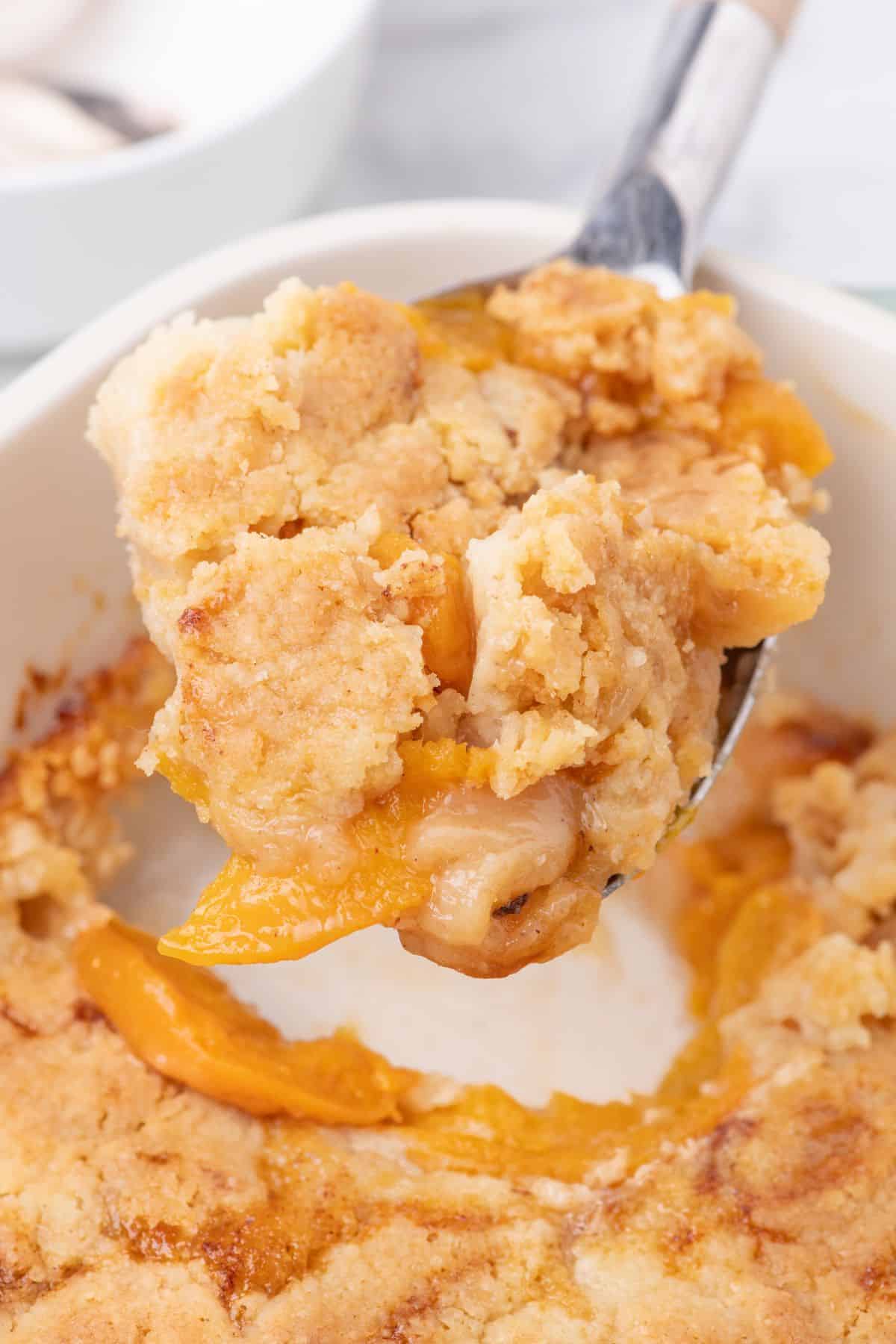 Close up view of a spoon scooping out a piece of peach dump cake.