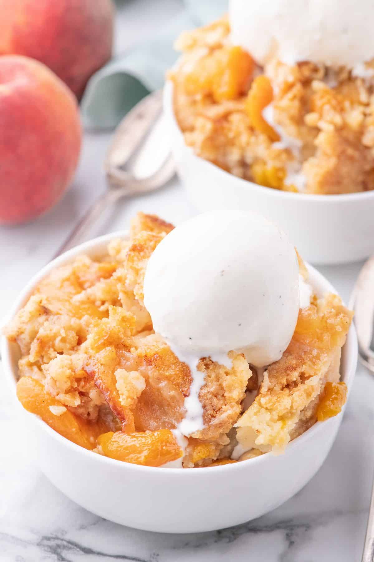 Peach cobbler with cake mix served in a bowl with vanilla ice cream on top.