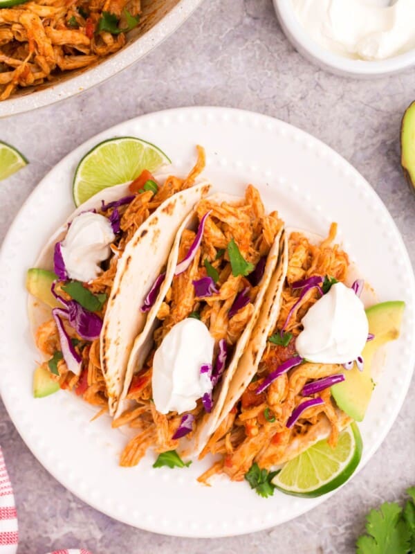 overhead picture of pulled chicken tacos on a white plate with limes