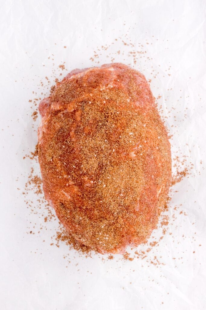 adding homemade seasoning to pork shoulder