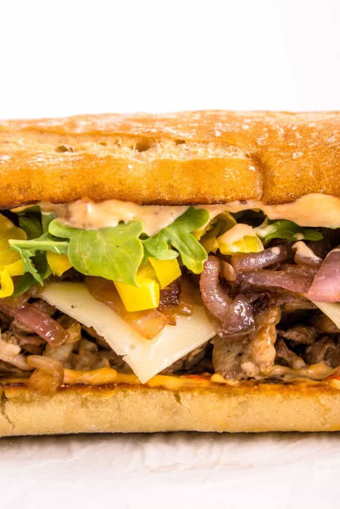 assembling a steak sandwich with meat, chipotle mayo and arugula