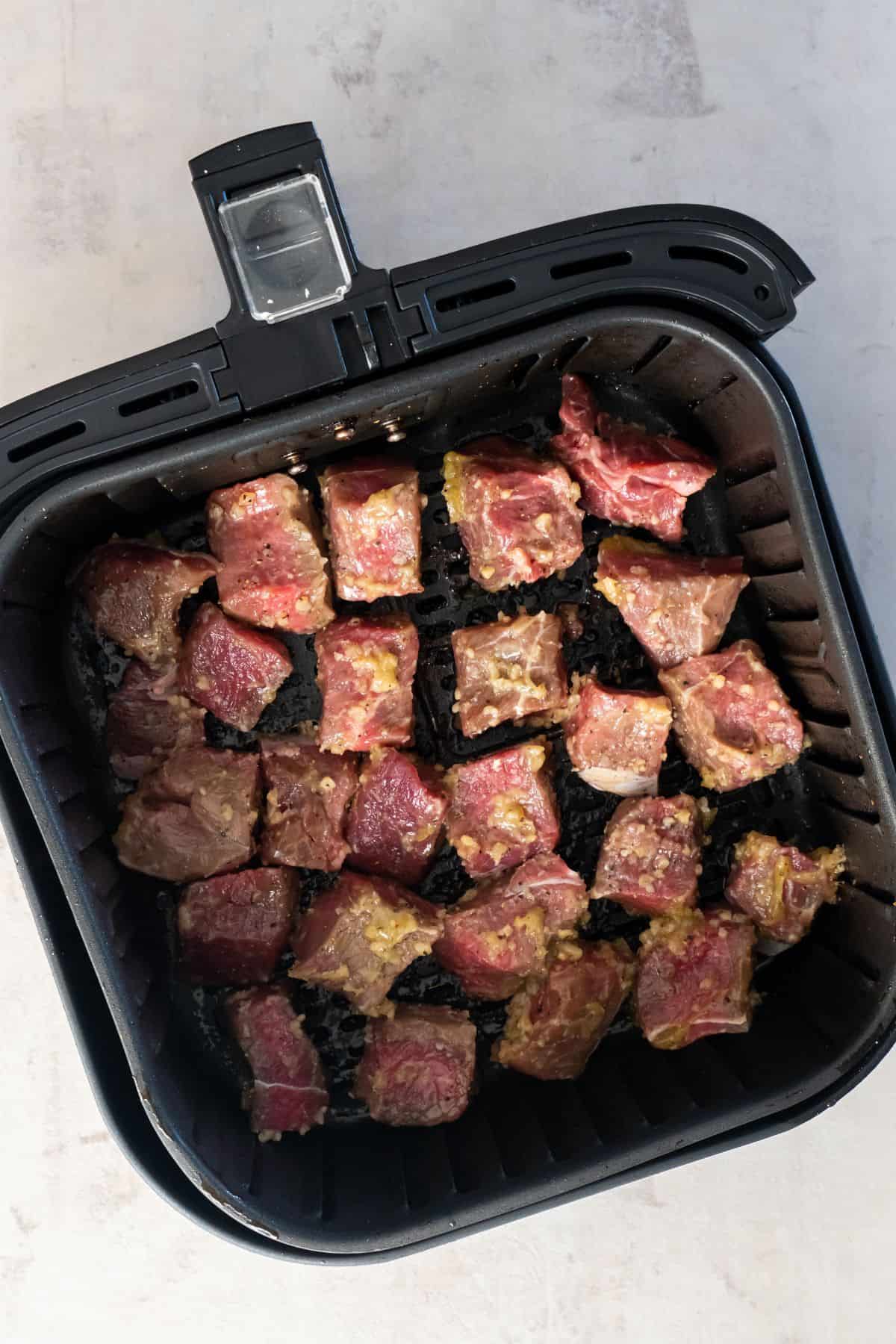 Raw steak bites in an air fryer basket.