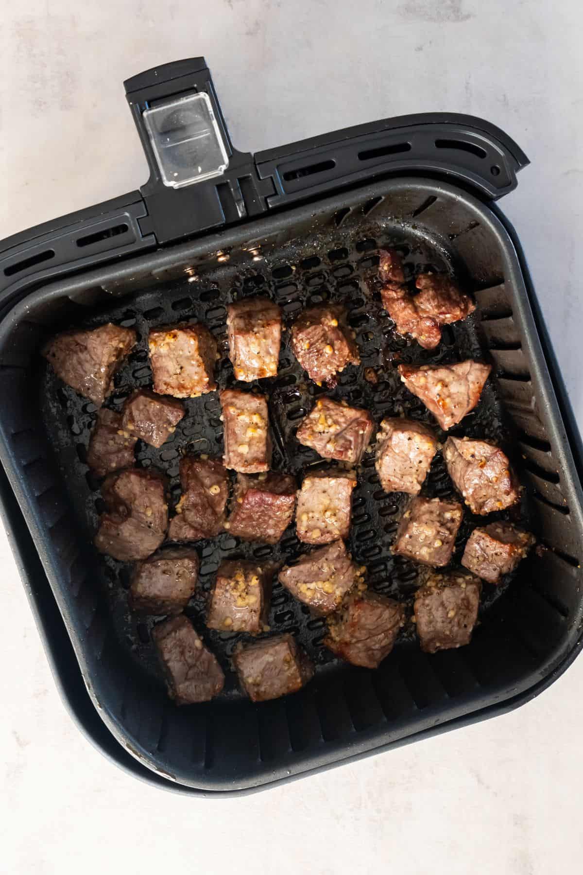 Cooked to medium rare steak bites in an air fryer basket.