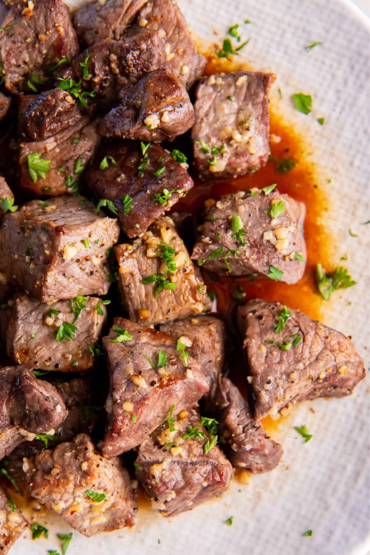 Steak bites with garlic butter sauce on them on a white plate.