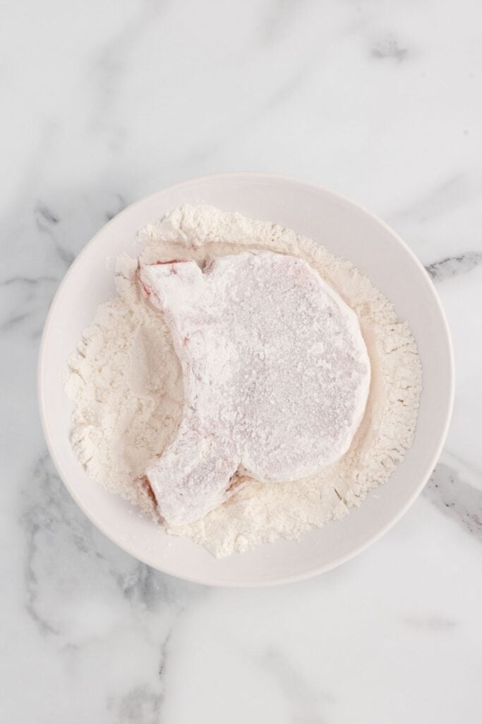 Pork chop being dredged in flour.