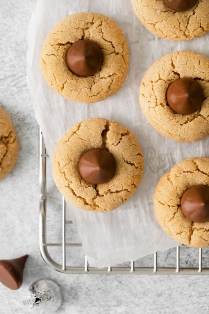 Peanut butter kiss cookies on parchment paper on a wire rack.