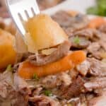 Fork full of potato, carrot, and chuck roast above a white plate.