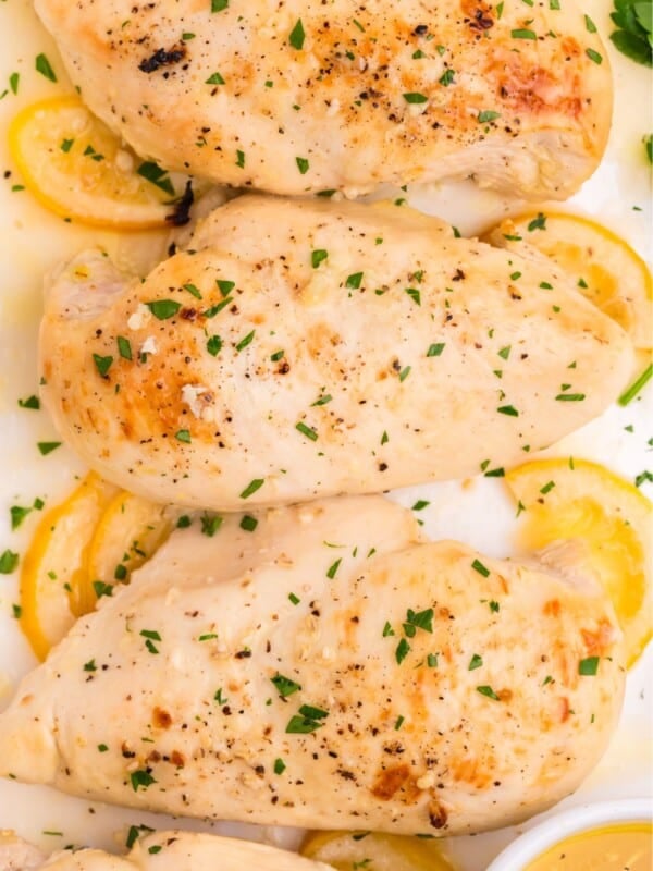 Lemon butter chicken with lemon slices on a white serving dish.