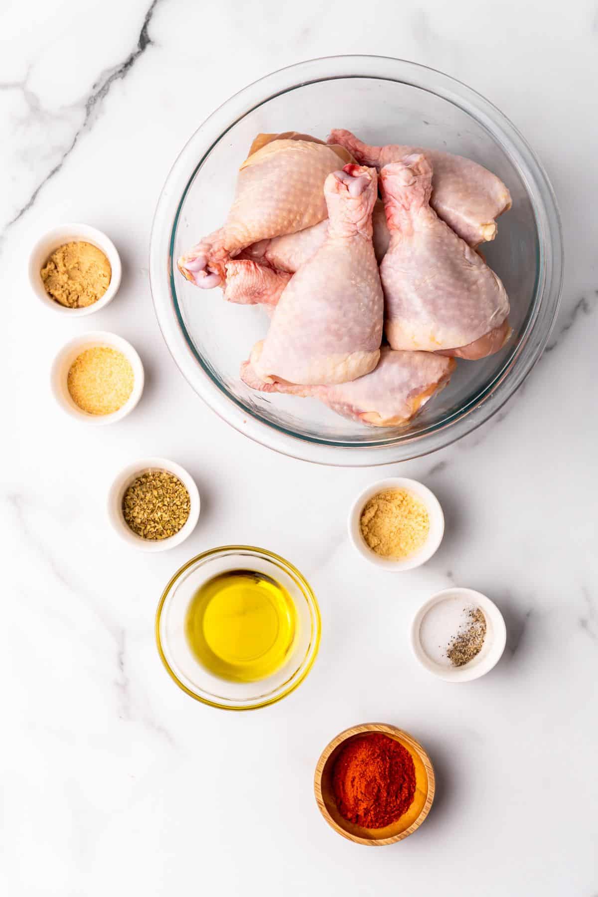 Ingredients needed to make chicken legs in the air fryer: chicken legs, oil, and seasonings in separate bowls.