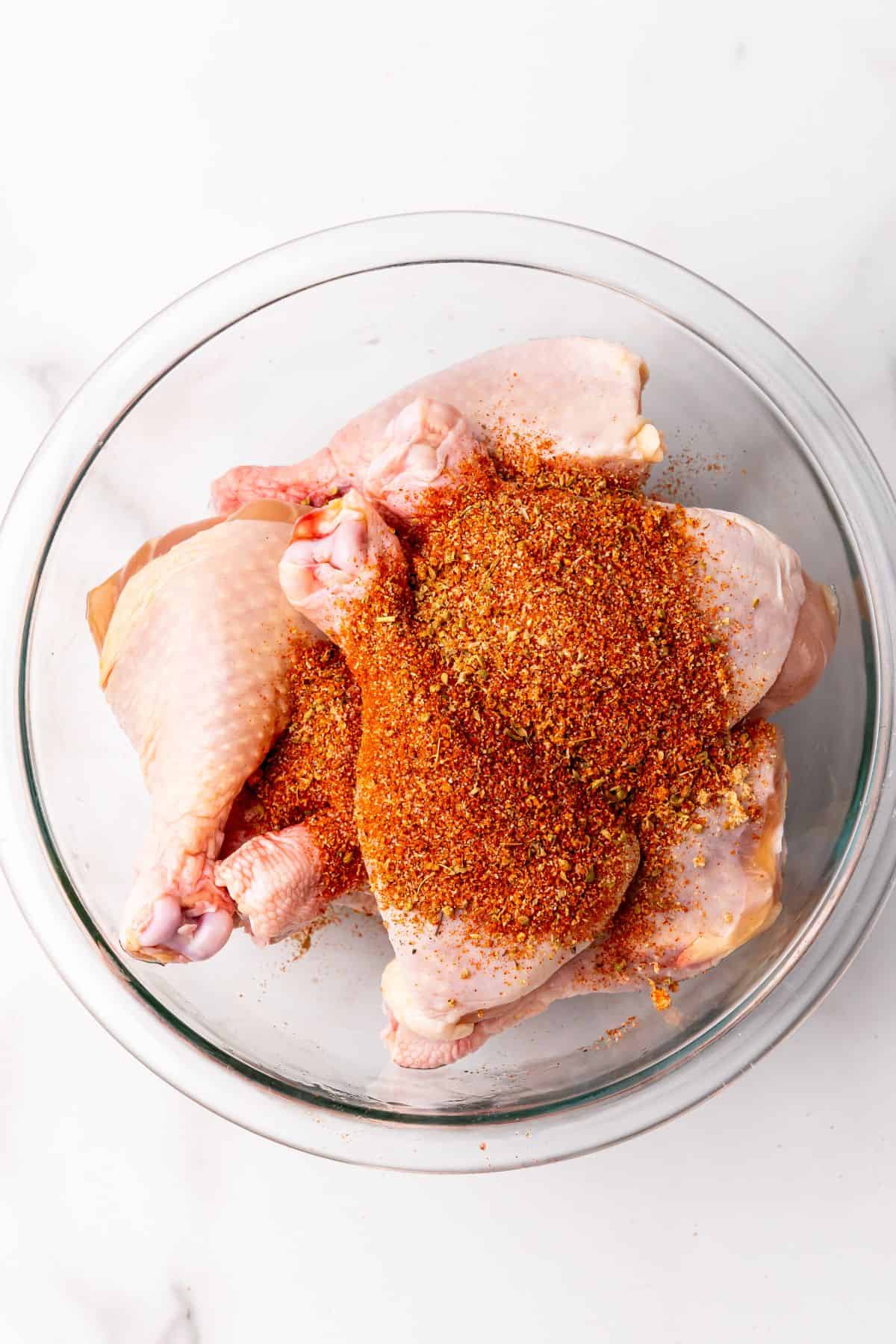 Chicken legs in a bowl with seasonings on top of them.