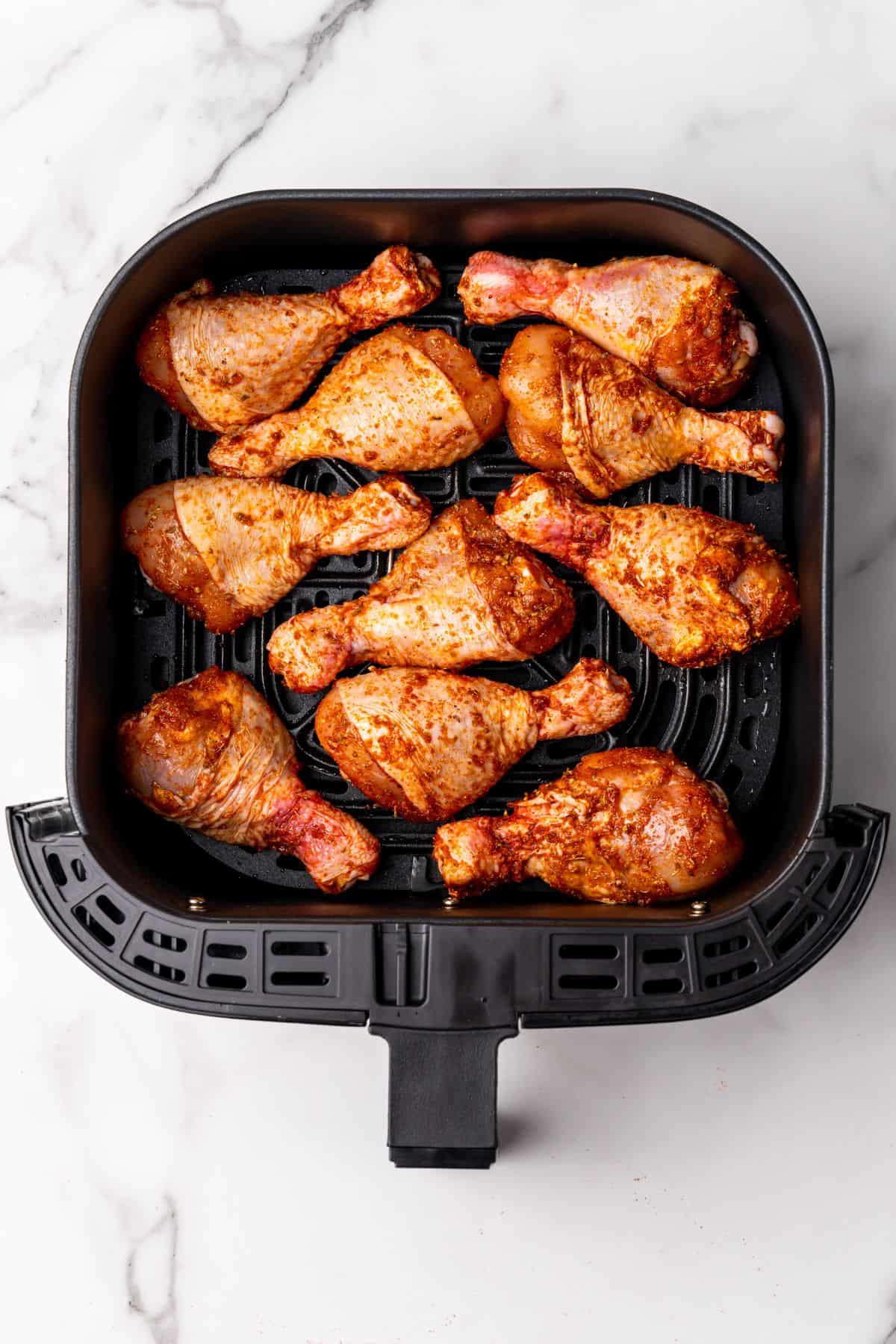 Raw chicken legs in an air fryer basket.