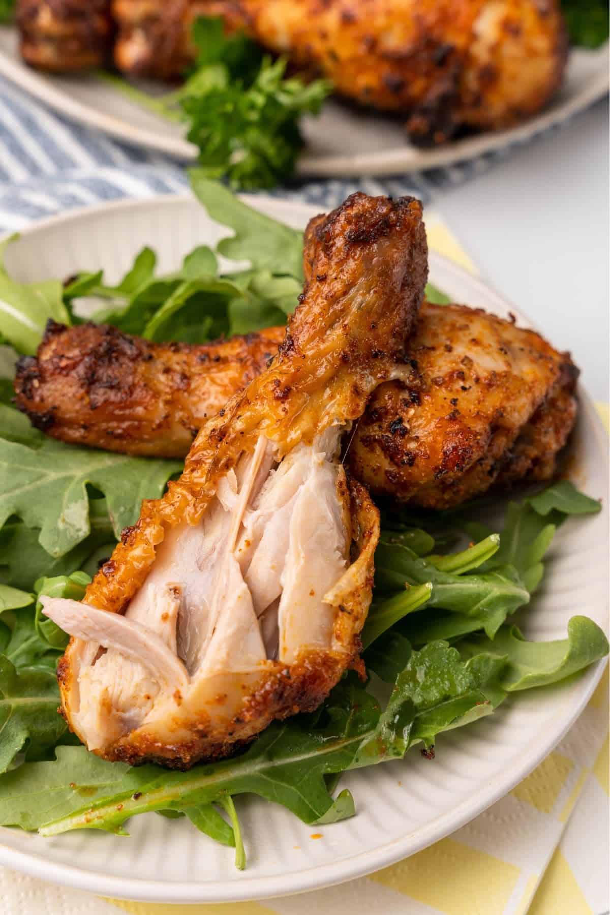 A chicken leg on a plate with lettuce with a bite taken out so you can see the juicy dark meat inside.