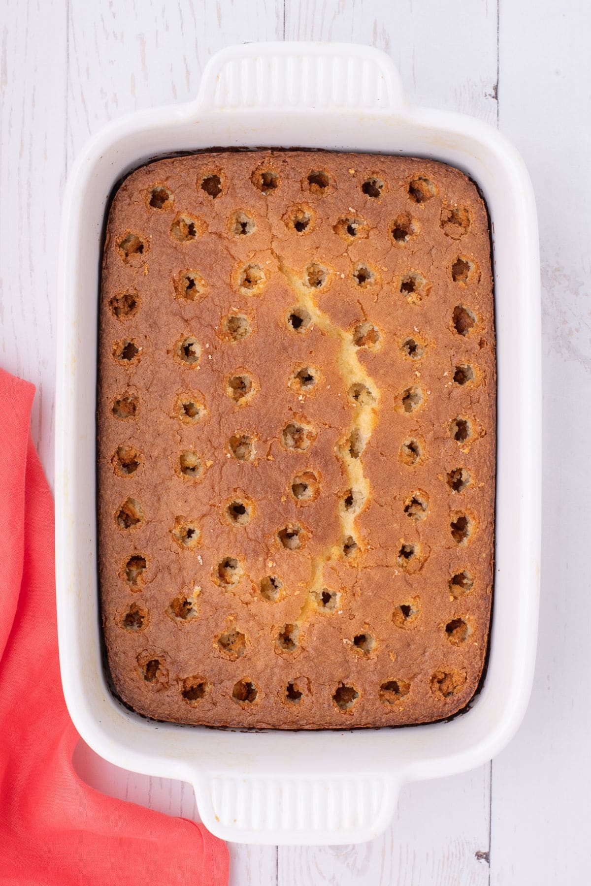 White cake with holes pierced into it about to be filled with jello.