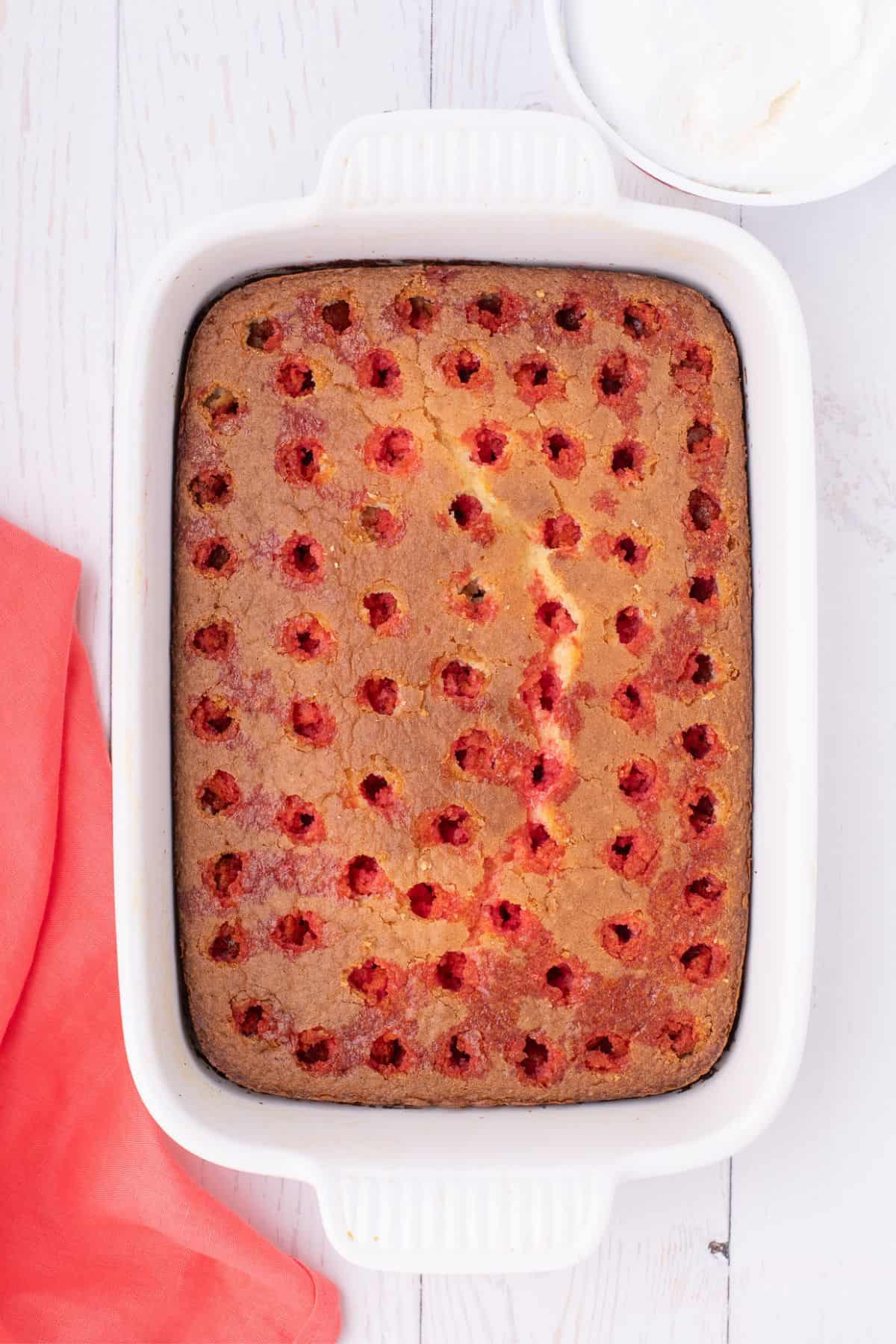 Strawberry jello poke cake with jello poured into the holes on the top of the cake.