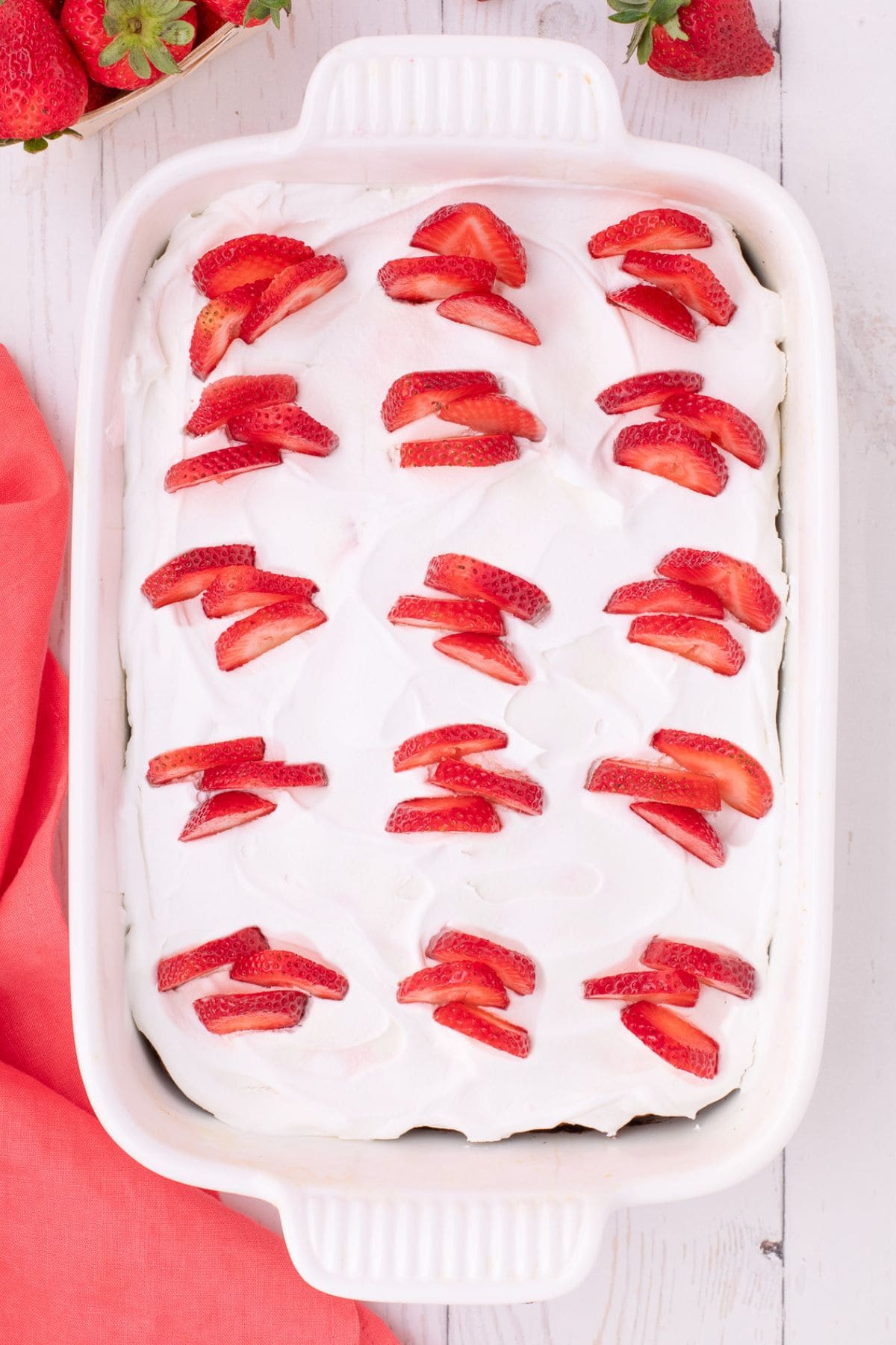 Overhead view of the poke cake topped with Cool Whip and sliced strawberries.