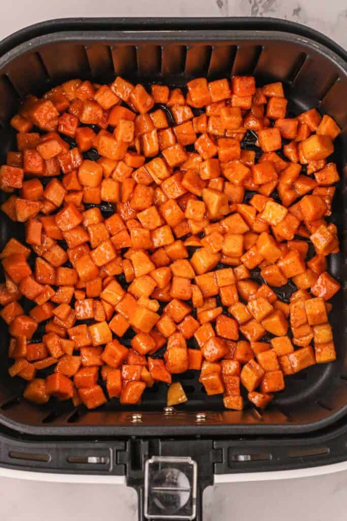 Raw butternut squash in an air fryer basket about to be cooked.
