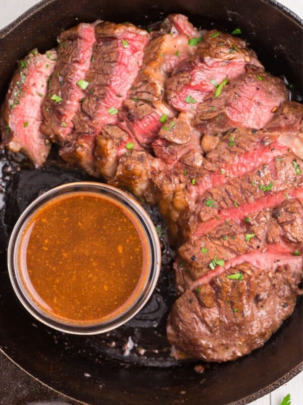 Overhead view of medium rare cooked steak that's sliced, next to a small bowl of easy steak marinade.